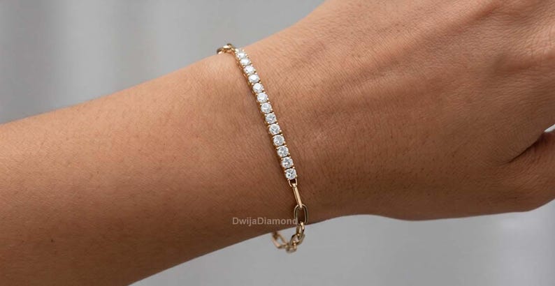 May include: A gold bracelet featuring a line of clear, round gemstones. The bracelet is worn on a wrist, with a small chain link clasp. This delicate piece of jewellery is a stylish accessory.