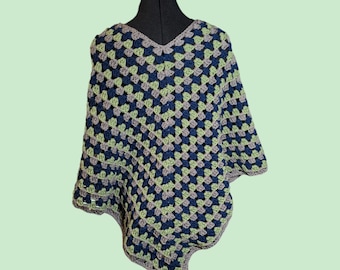 Puede incluir: Un poncho tejido a crochet con un patrón geométrico en tonos de azul, verde y gris. El poncho tiene un cuello en V y un borde con flecos.