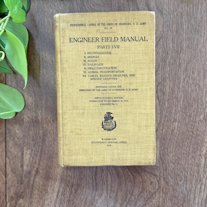May include: A tan hardcover book titled Engineer Field Manual Parts I-VII, Professional Papers of the Corps of Engineers, U.S. Army, Fifth Revised Edition, 1918, featuring a black emblem and text detailing reconnaissance, bridges, and roads.