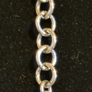 Puede incluir: Una cadena plateada con un dije en forma de coraz&oacute;n. El dije tiene un dise&ntilde;o grabado y est&aacute; conectado a la cadena por un peque&ntilde;o anillo. La cadena est&aacute; hecha de varios eslabones ovalados.