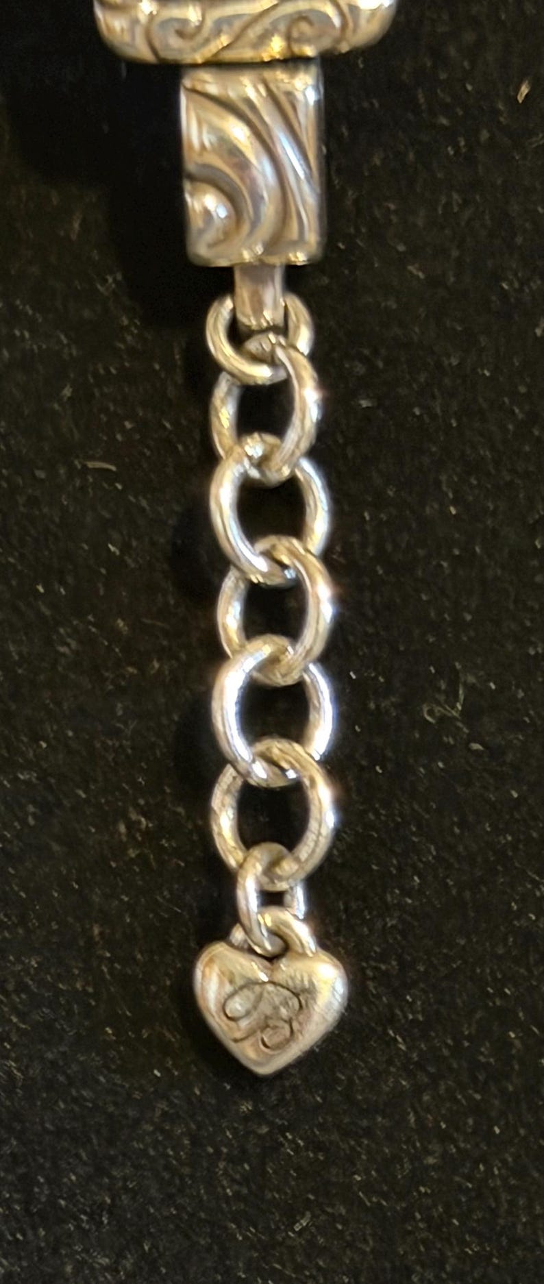 Puede incluir: Una cadena plateada con un dije en forma de coraz&oacute;n. El dije tiene un dise&ntilde;o grabado y est&aacute; conectado a la cadena por un peque&ntilde;o anillo. La cadena est&aacute; hecha de varios eslabones ovalados.