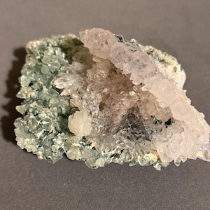 May include: A mineral specimen featuring a cluster of translucent, pale lavender crystals layered over a base of small, textured, sea-green crystals. The formation has an irregular, jagged shape with varying crystal sizes and a crystalline surface.