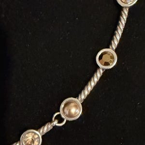 May include: Silver-toned necklace with a twisted rope design. The necklace features several round, champagne-colored gemstones set in silver bezels. The gemstones are evenly spaced along the chain, creating a delicate and elegant look.