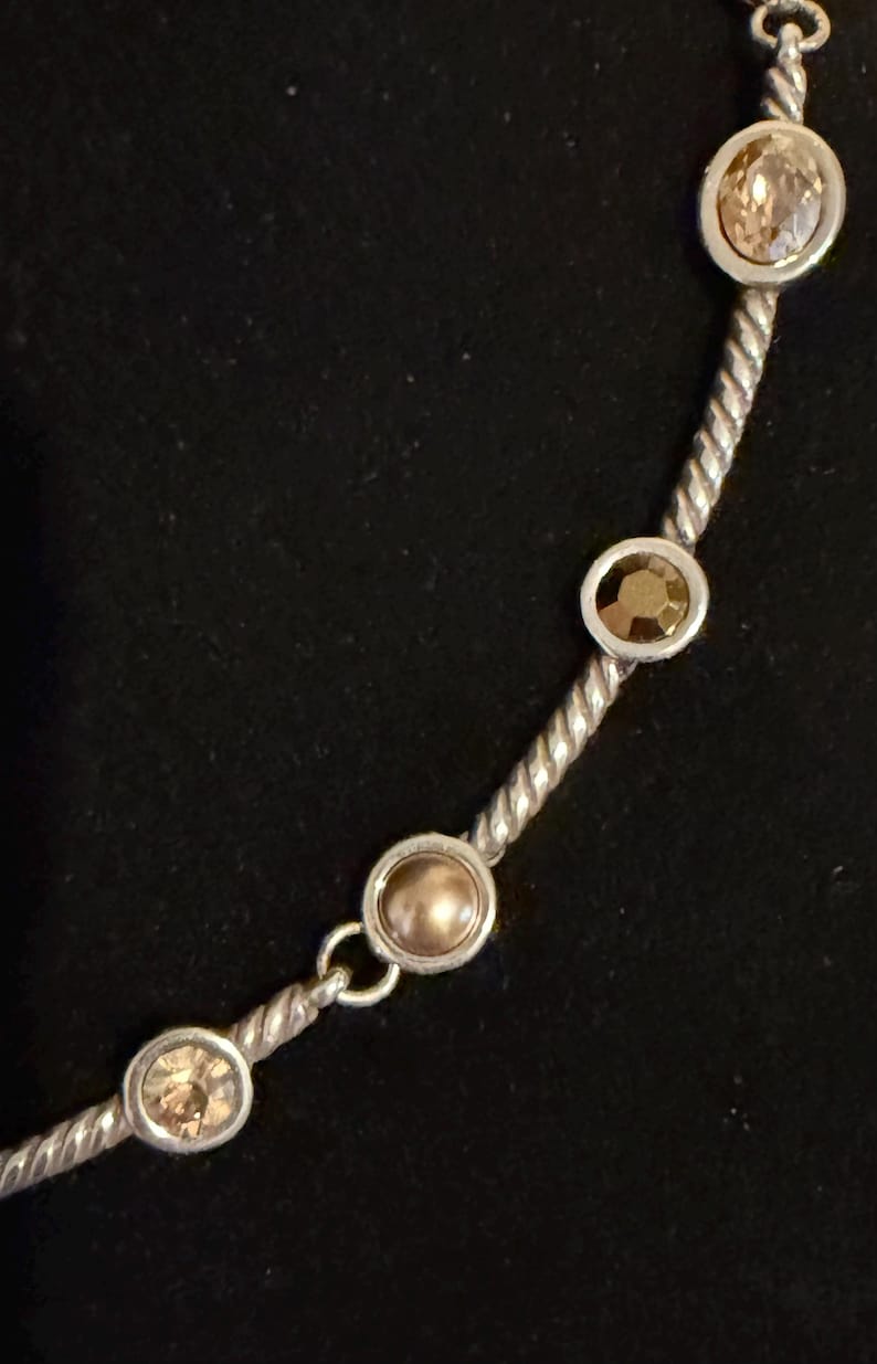 May include: Silver-toned necklace with a twisted rope design. The necklace features several round, champagne-colored gemstones set in silver bezels. The gemstones are evenly spaced along the chain, creating a delicate and elegant look.