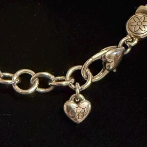 Może przedstawiać: Srebrny naszyjnik z zawieszką w kształcie serca i zapięciem w kształcie kwiatu. Zawieszka ma grawerowany wz&oacute;r, a naszyjnik ma okrągłe ogniwa. Zapięcie jest w stylu karabińczyka.