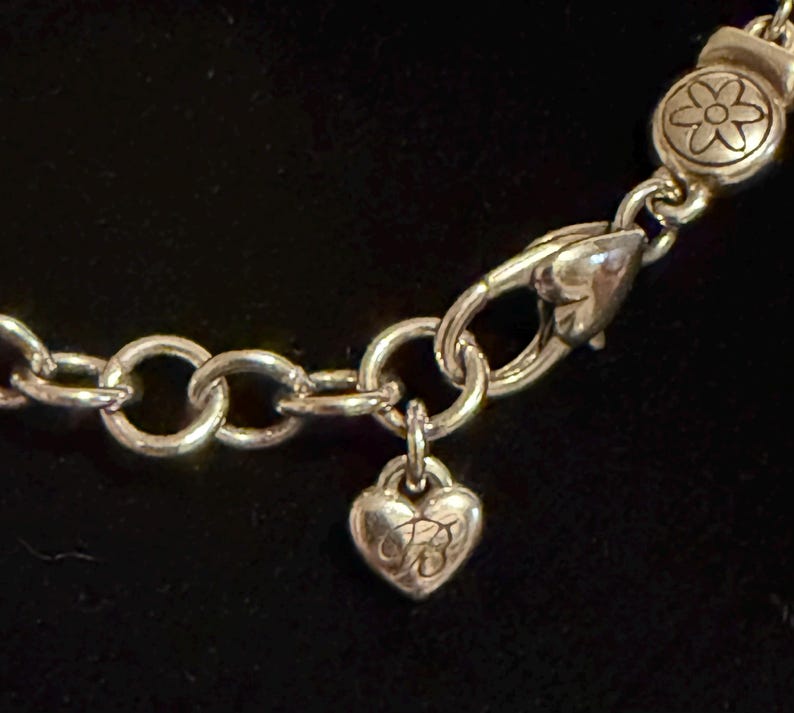 Może przedstawiać: Srebrny naszyjnik z zawieszką w kształcie serca i zapięciem w kształcie kwiatu. Zawieszka ma grawerowany wz&oacute;r, a naszyjnik ma okrągłe ogniwa. Zapięcie jest w stylu karabińczyka.