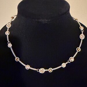 May include: Silver-toned necklace with alternating clear and champagne-colored round gemstones. The gemstones are set along a twisted silver chain. The necklace is displayed on a black mannequin.
