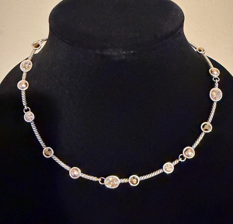 May include: Silver-toned necklace with alternating clear and champagne-colored round gemstones. The gemstones are set along a twisted silver chain. The necklace is displayed on a black mannequin.