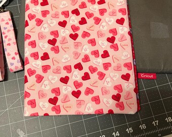 May include: A pink fabric pouch with a heart pattern featuring the words "XOXO", "LOVE", and "SWEET". The pouch is on a gray cutting mat with a ruler.
