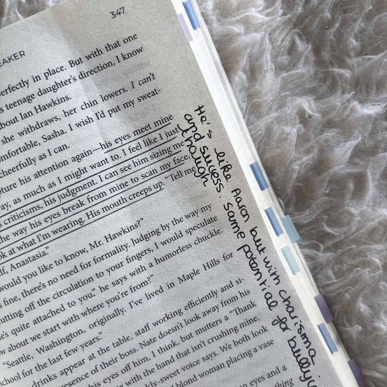 May include: A page from a printed book with black text on white paper, featuring handwritten notes in black ink in the margin. The page includes page number 347 and several light blue and purple adhesive page markers attached to the outer edge.