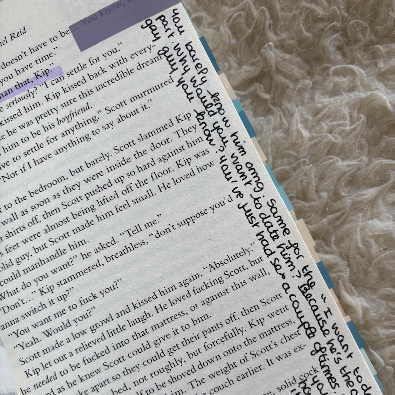 May include: Open book with text and handwritten notes in black ink. The text includes phrases like "I can settle for you" and "You want me to fuck you?" The book has blue and purple page markers.