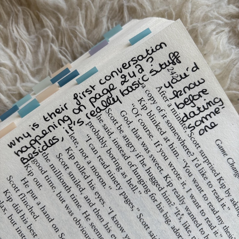 May include: Close-up of a book's open pages with handwritten notes and highlighted tabs. The text includes phrases like "first conversation," "page 242," and "really basic stuff." The tabs are in shades of blue and beige.