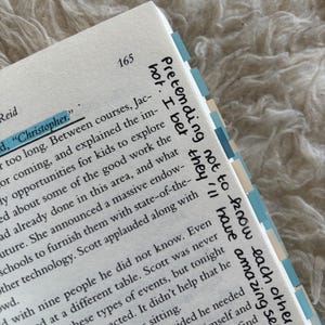 May include: Open book page with text and highlighted words. The page number 165 is visible. The text includes the words "Christopher" and "Pretending not to know each other". The book has blue and white page markers.