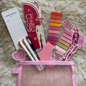 May include: A pink pencil case containing stationery. The contents include pens, sticky notes, bookmarks, and stickers with phrases such as "Pink Pony Book Club" and "Falling for a Villain Again." The items are displayed on a fluffy, white surface.