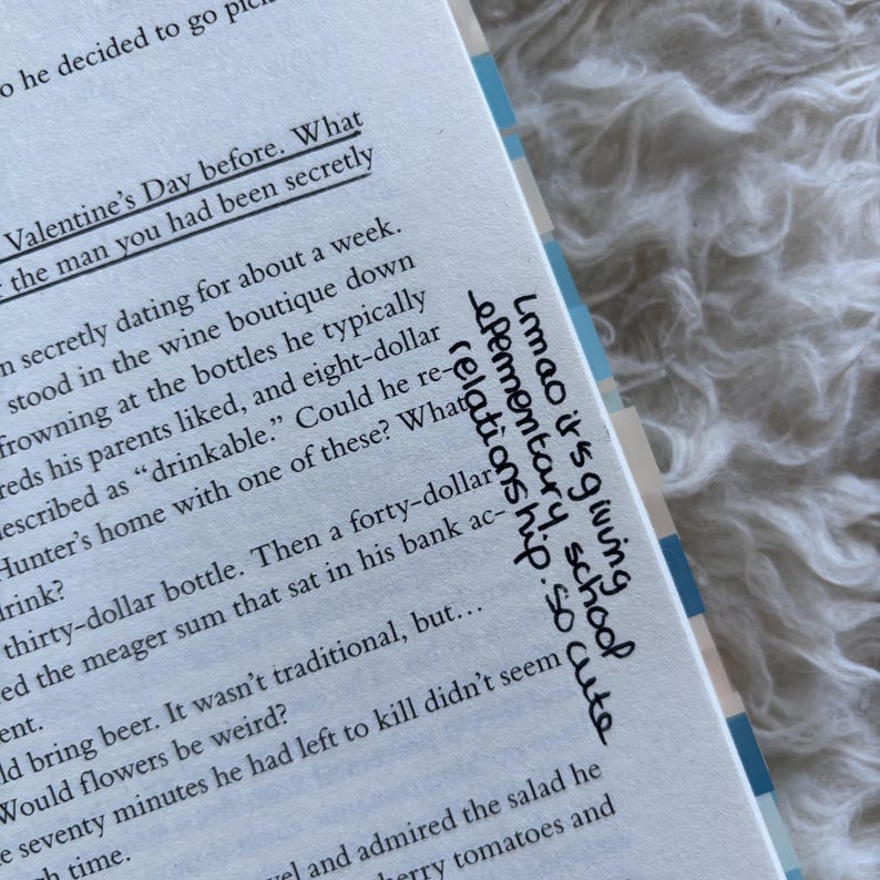May include: Open book with printed text and handwritten notes. The text includes phrases like "Valentine's Day before" and "drinkable." Handwritten text says "Lmao it's giving elementary school relationship. so cute."
