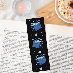 Op de afbeelding: Zwarte boekenlegger met een herhalend patroon van blauwe cadeau dozen en sneeuwvlokken. De boekenlegger ligt op een open boek met tekst zichtbaar.