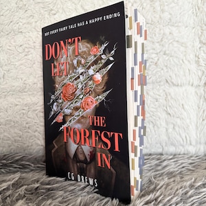 May include: A hardback book titled "Don't Let the Forest In" by CG Drews. The cover is dark with red text and a surreal illustration of a face with roses and thorns. The book's pages have colourful tabs.