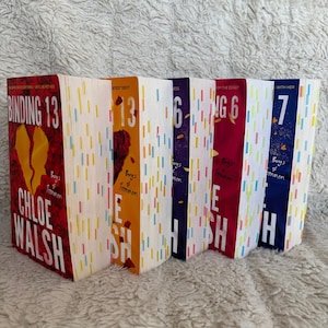 May include: A collection of six books with colorful covers. The books have titles like "Binding 13" and "13". The author's name, Chloe Walsh, is visible on one book. The spines are white with vertical stripes of various colors.