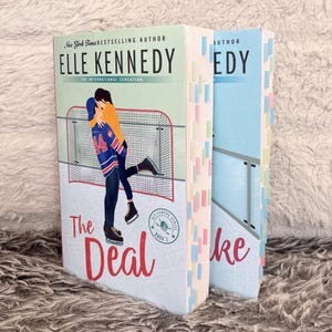 May include: Two paperback books by Elle Kennedy titled The Deal and another book from the Off-Campus series. The covers feature illustrations of two people embracing on ice skates in front of a hockey net. Both books have colorful page markers.