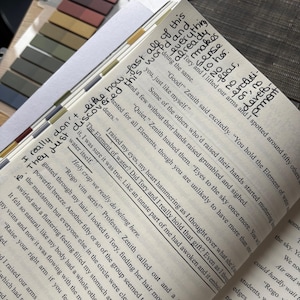 Puede incluir: Libro abierto con notas manuscritas y pasajes resaltados. Se pueden leer frases como "The Element of water?" y "Holy crap we really do belong here". Notas adhesivas de colores son visibles en el lateral de las p&aacute;ginas.