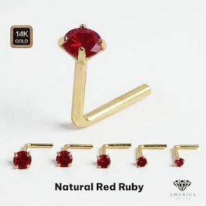 May include: A collection of gold nose studs with natural red ruby gemstones. The studs vary in size, with an L-shaped post. The image includes a close-up of a single stud and the text "Natural Red Ruby".