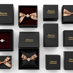 May include: An overhead shot of several black jewelry boxes, some open to reveal rings and gemstones. The boxes are adorned with gold bows and the words "America Gemstones" in gold lettering. The interiors of the boxes are lined with red or black fabric.