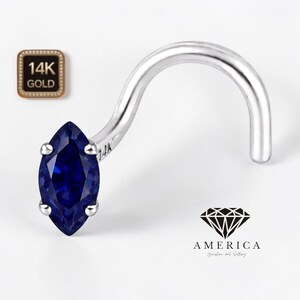 May include: A silver nose ring with a marquise-cut, deep blue gemstone. The jewelry is marked with "14K" and a diamond logo with the word "AMERICA" below it. The nose ring has a curved design.
