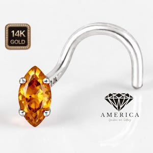 May include: A nose ring with a marquise-cut, golden-yellow gemstone. The curved post is silver-colored, and the setting is accented with small silver prongs. The image also includes a 14K gold stamp.