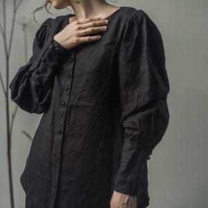 Peut inclure: Une chemise noire à manches longues boutonnée avec des manches bouffantes et une coupe ample.