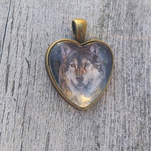 May include: A heart-shaped pendant with a wolf's face image inside. The pendant is made of metal with a bronze finish.