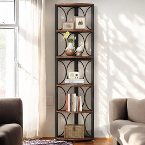 May include: A brown corner shelf unit with a black metal frame and circular accents. The shelf has five shelves and is decorated with a vase of flowers, books, and a small radio.