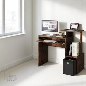 May include: A dark brown wooden desk with a pull-out keyboard tray and a shelf unit. The desk has a laptop on the top shelf, a computer monitor on the desk, and a black storage bin on the bottom shelf. The desk is in a room with white walls and a window.