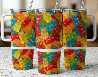 May include: Three stainless steel tumblers with white handles and lids. Each tumbler is covered in a colorful pattern of gummy bear candies in red, orange, yellow, green, and blue. The tumblers have silver straws.
