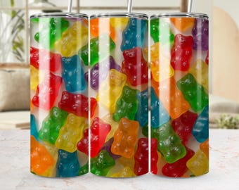 May include: A set of three stainless steel tumblers with a vibrant, colorful design. The tumblers are covered in a pattern of gummy bear candies in various colors, including red, yellow, green, blue, and orange. Each tumbler has a silver straw.
