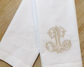 May include: Two white linen hand towels with embroidered initials. The towel on the left has a white embroidered "A" and the towel on the right has a gold embroidered "L".