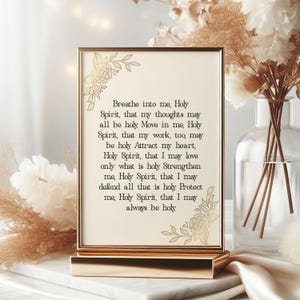 May include: A rectangular gold-framed sign featuring the text: Breathe into me, Holy Spirit, that my thoughts may all be holy. Move in me, Holy Spirit, that my work, too, may be holy. Attract my heart, Holy Spirit, that I may love only what is holy.