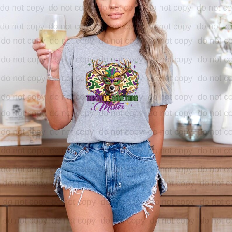 A woman wearing a gray t-shirt with a colorful graphic design and denim shorts is holding a glass of wine.