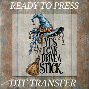 May include: A DTF transfer design featuring a blue witch hat with a brown belt, gold bells, and a broomstick. The text reads: READY TO PRESS, YES I CAN DRIVE A STICK, and DTF TRANSFER. The illustration includes gold stars and crescent moon accents.