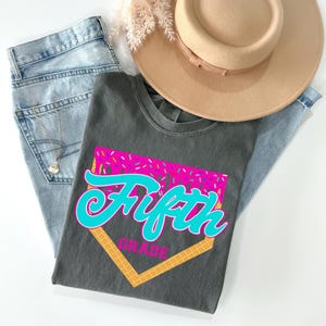 a gray t-shirt with a graphic design, a pair of jeans, and a beige hat, all laid out on a white background.