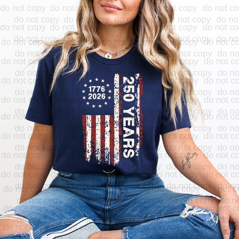 A woman wearing a navy blue t-shirt with a graphic design featuring the American flag and the text "1776 2026 250 YEARS" printed on it.