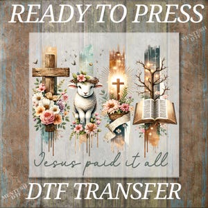 May include: A ready-to-press DTF transfer design featuring a white lamb with a crown of thorns, a cross, a Bible, and flowers. The text "Jesus paid it all" is written below the design.