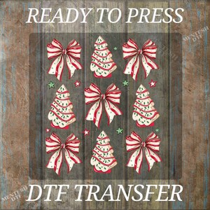 May include: A DTF transfer design featuring Christmas bows and Christmas trees with red and white stripes and green accents. The words "READY TO PRESS" and "DTF TRANSFER" are printed in white.