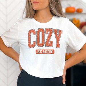 A woman wearing a white t-shirt with the text "COZY SEASON" printed on it.