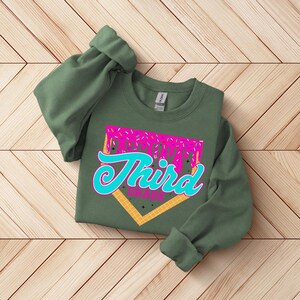 A green sweatshirt with a graphic design on it, featuring the text "Third Grade" in a stylized font.