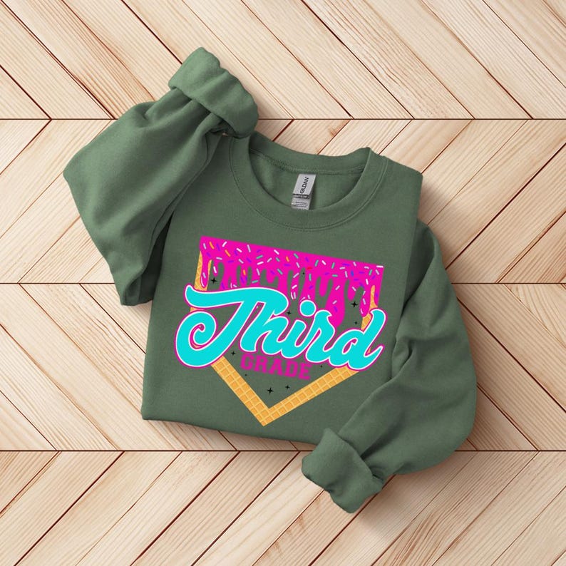 A green sweatshirt with a graphic design on it, featuring the text "Third Grade" in a stylized font.