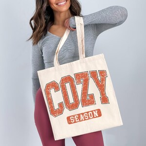 A woman holding a large tote bag with the word "COZY" printed on it.