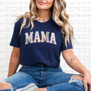 A woman wearing a navy blue t-shirt with the word "MAMA" printed on it, sitting on the ground with her legs crossed.
