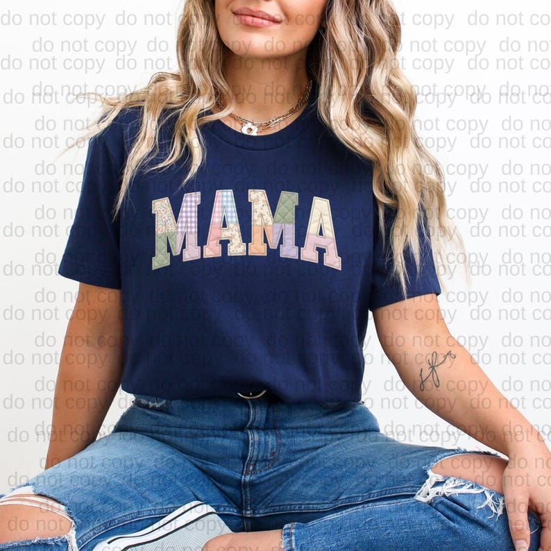 A woman wearing a navy blue t-shirt with the word "MAMA" printed on it, sitting on the ground with her legs crossed.