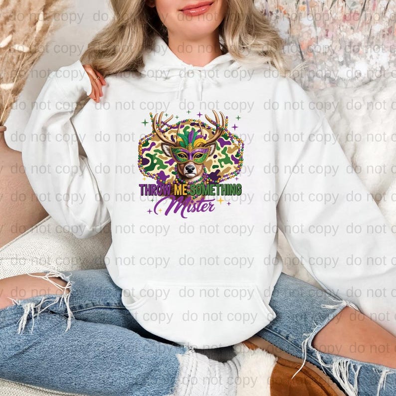 A woman wearing a white hoodie with a colorful graphic design of a deer head and the text "THROW ME SOMETHING MISTER" printed on it.