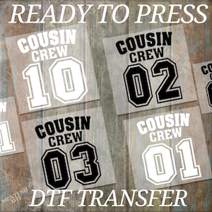 May include: DTF transfers with the text "READY TO PRESS" at the top. The transfers feature the words "COUSIN CREW" above the numbers 10, 02, 03, and 01. The bottom of the image reads "DTF TRANSFER".